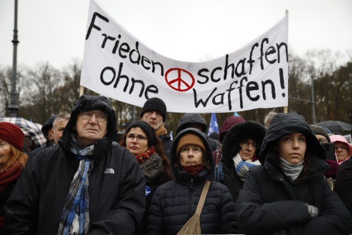 People hold up a banner that says ‘Make peace without weapons’ during a demonstration against war and arming in Berlin at the Brandenburg Gate in 2023 