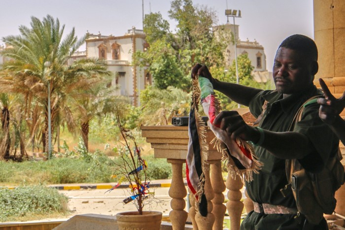 A Sudan army soldier holds a national flag to celebrate after the army take over the Republican Palace in Khartoum