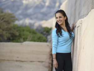 Paula standing outside by a wall wearing a blue shirt