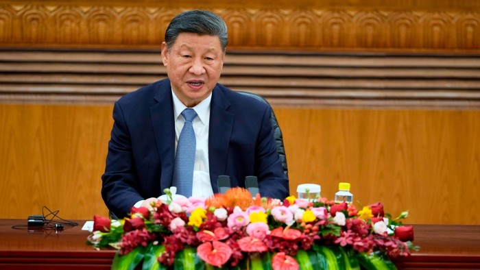 Xi Jinping is seated at a table adorned with a colourful floral arrangement