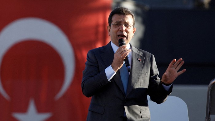 Ekrem İmamoğlu speaks at a rally with a large Turkish flag in the background