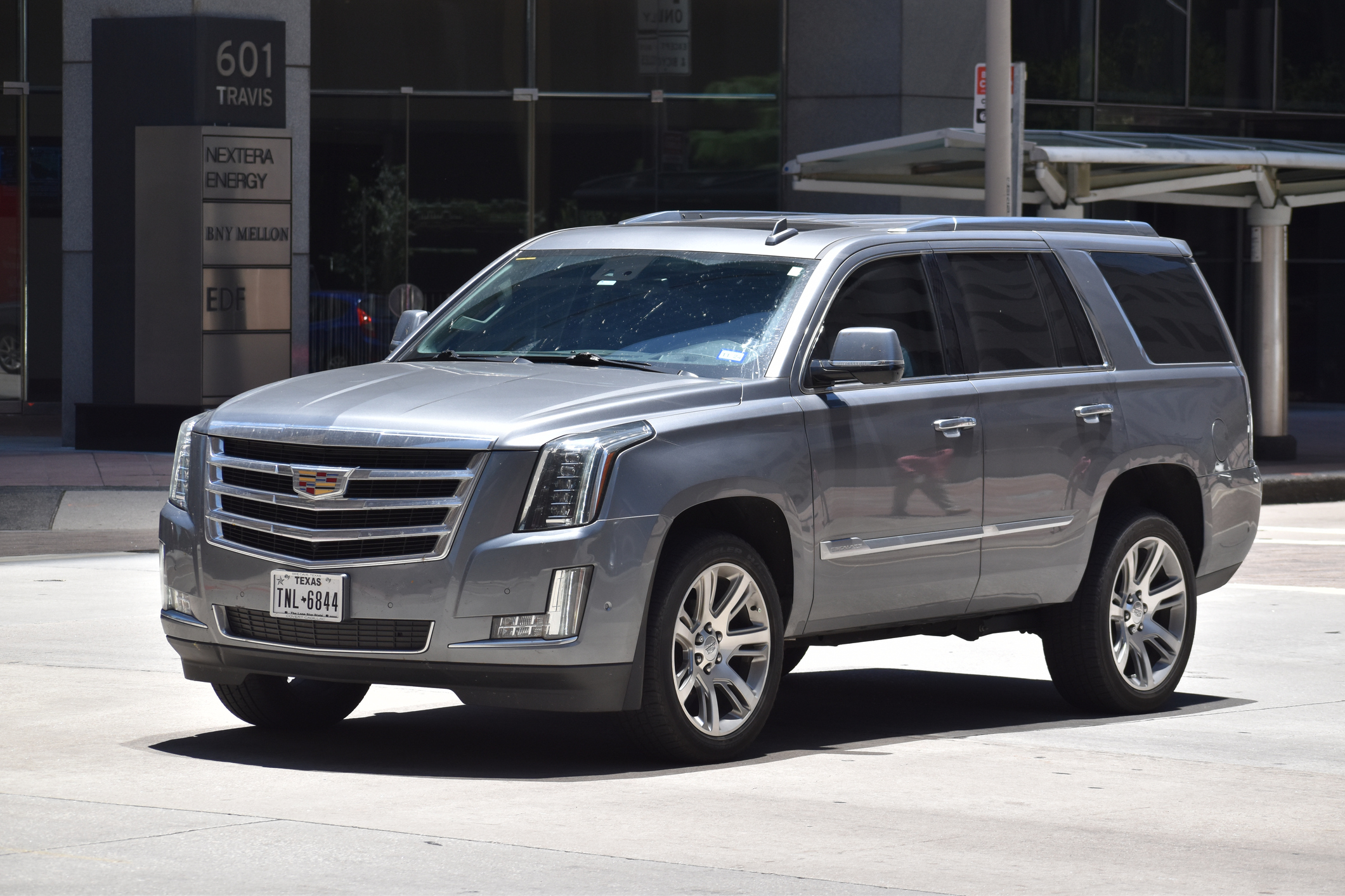 A silver Cadillac Escalade driving down a city street.