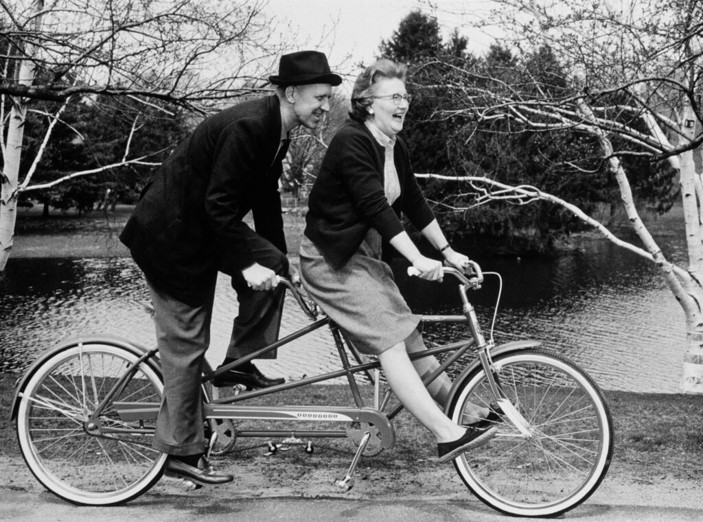 Retired couple riding a tandem bike in the 1960s.