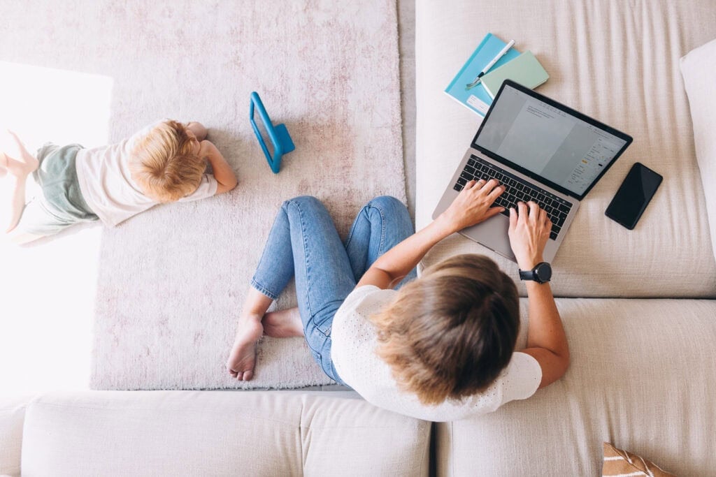 mom on laptop with child nearby - Where to sell used baby items
