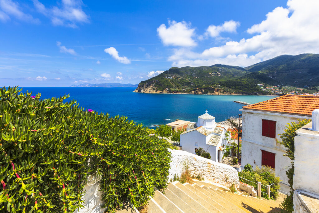 A view of stairs leading to a traditional Greek village, with azure blue water in the background, on the island of Skopolos in Greece.