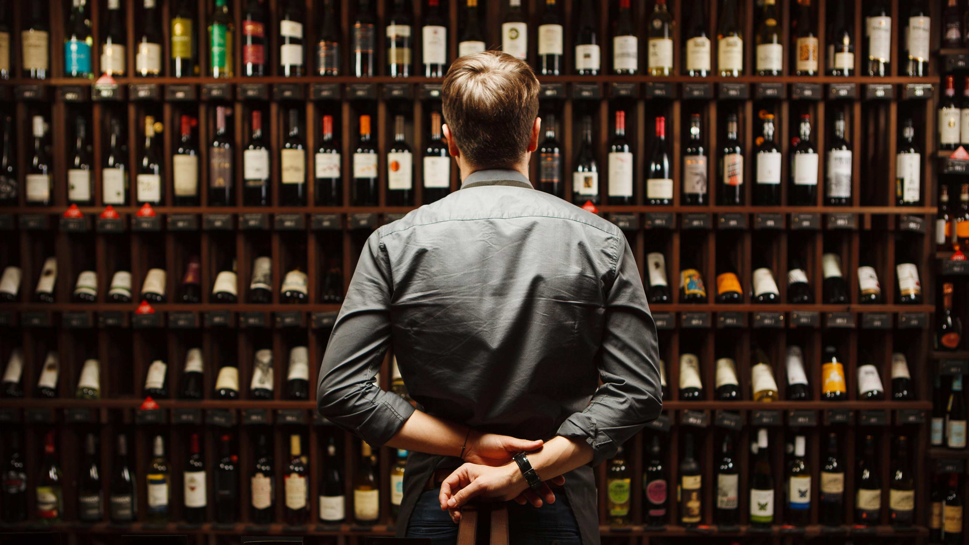 A wine sommelier at a restaurant looks at a wall full of bottles.