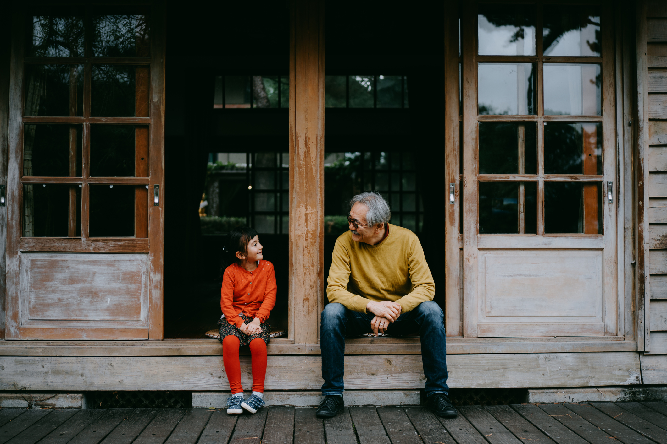 Portrait of Japanese grandfather and cute preschool granddaughter sitting on patio and smiling at each other