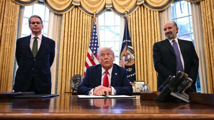 Donald Trump is seated at a desk in the Oval Office, speaking to the press. To his left is Treasury secretary Scott Bessent and to his right is commerce secretary Howard Lutnick