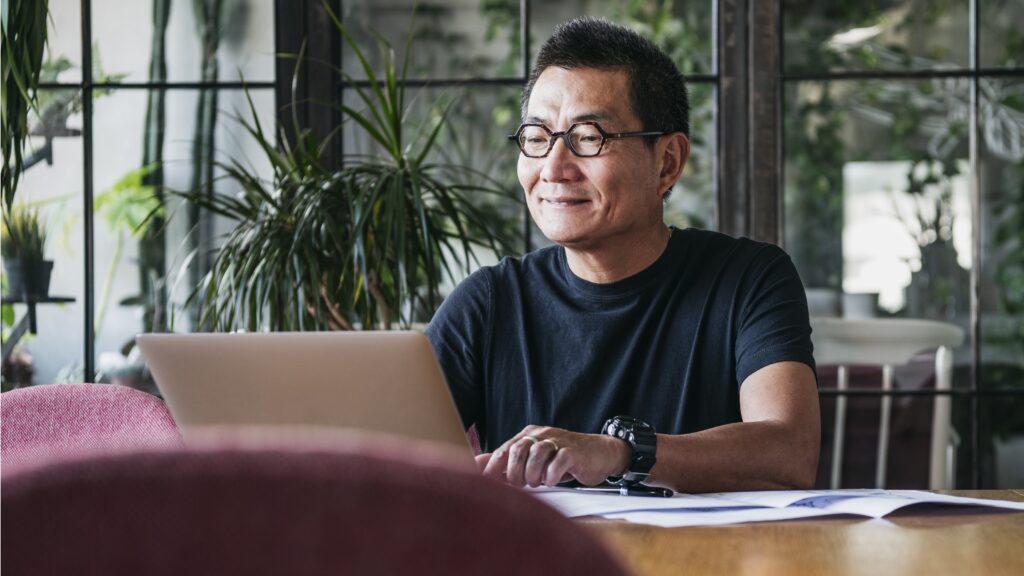 A man works on financial planning on his laptop at his dining room table.