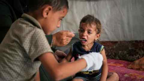 A little boy is fed by his mother with food from a community kitchen at the Muwasi camp for displaced Palestinians in Khan Younis, southern Gaza Strip
