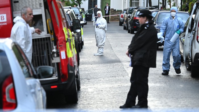 The three forensics officers are wearing white and blue overalls. A uniformed officer is also on duty