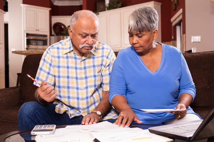 A seated couple examining bills and financial statements laid out on a table in front of them.
