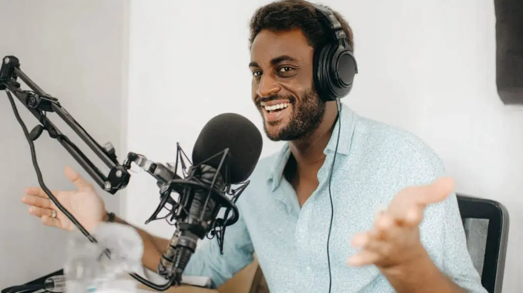 Smiling man with headphones speaks into a professional microphone, gesturing while podcast hosting.