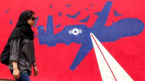 A woman walks past a mural painted on the outer walls of the former US embassy in Tehran