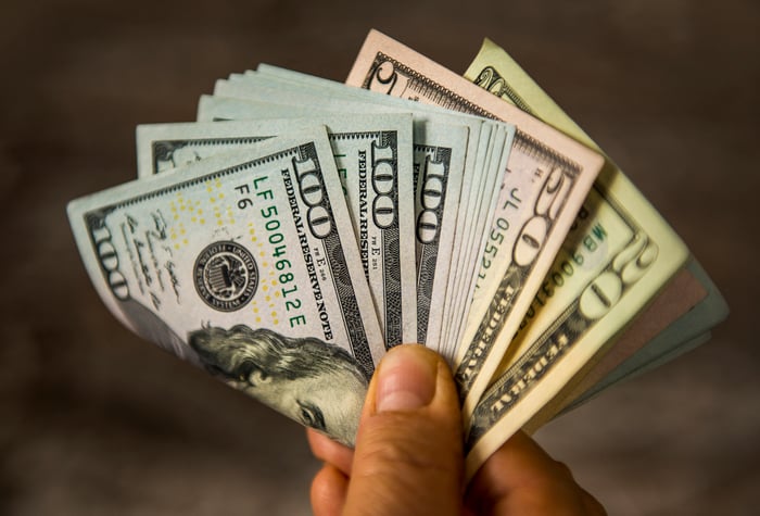 A person holding a fanned and folded assortment of cash bills by their fingertips.