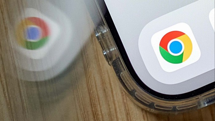 The Google Chrome app icon displayed on a smartphone screen, with its reflection visible on a wooden surface.