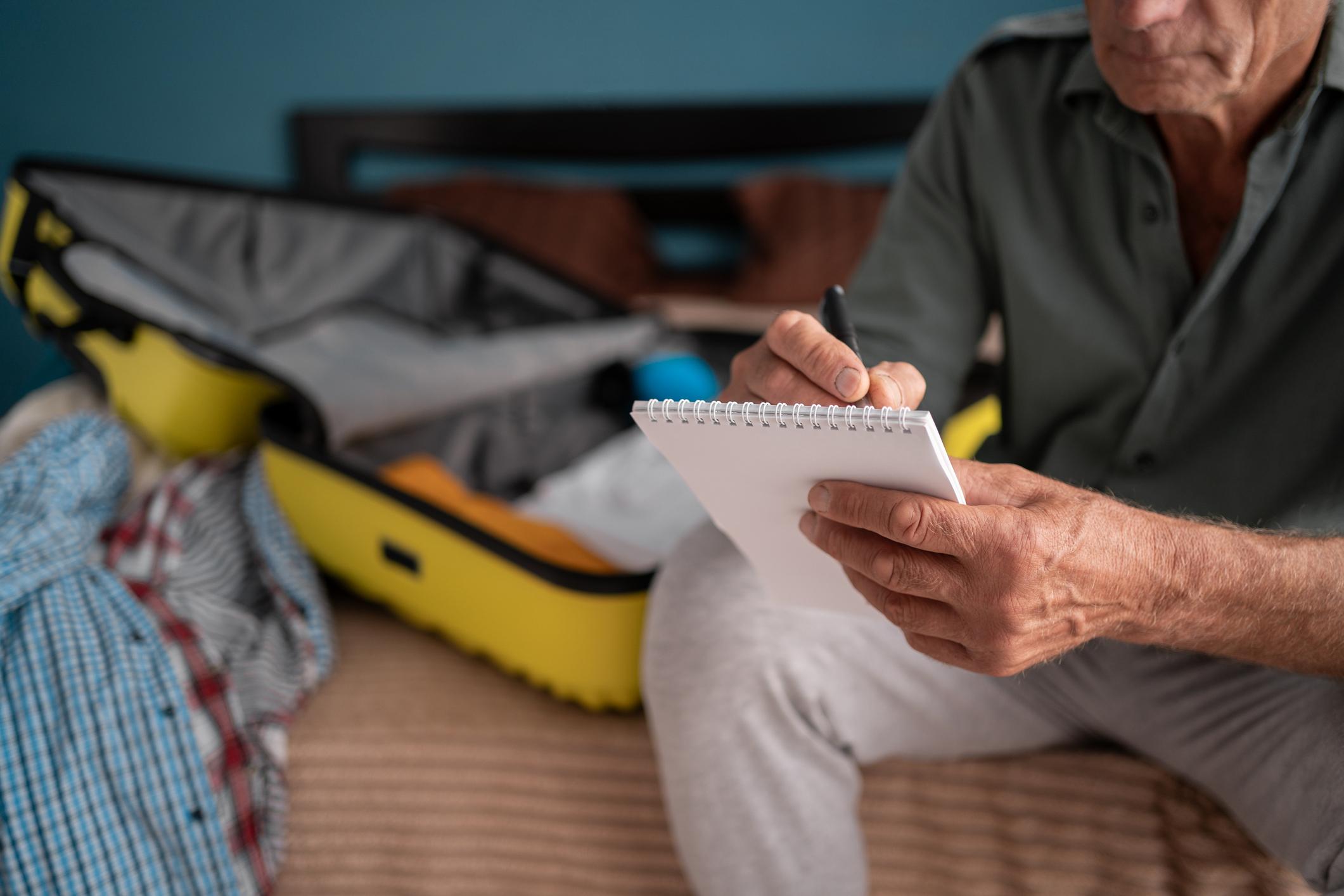 Vacation, holiday and travel concept. Man writing check list note after packing luggage or baggage for journey trip sitting at home. Copy space