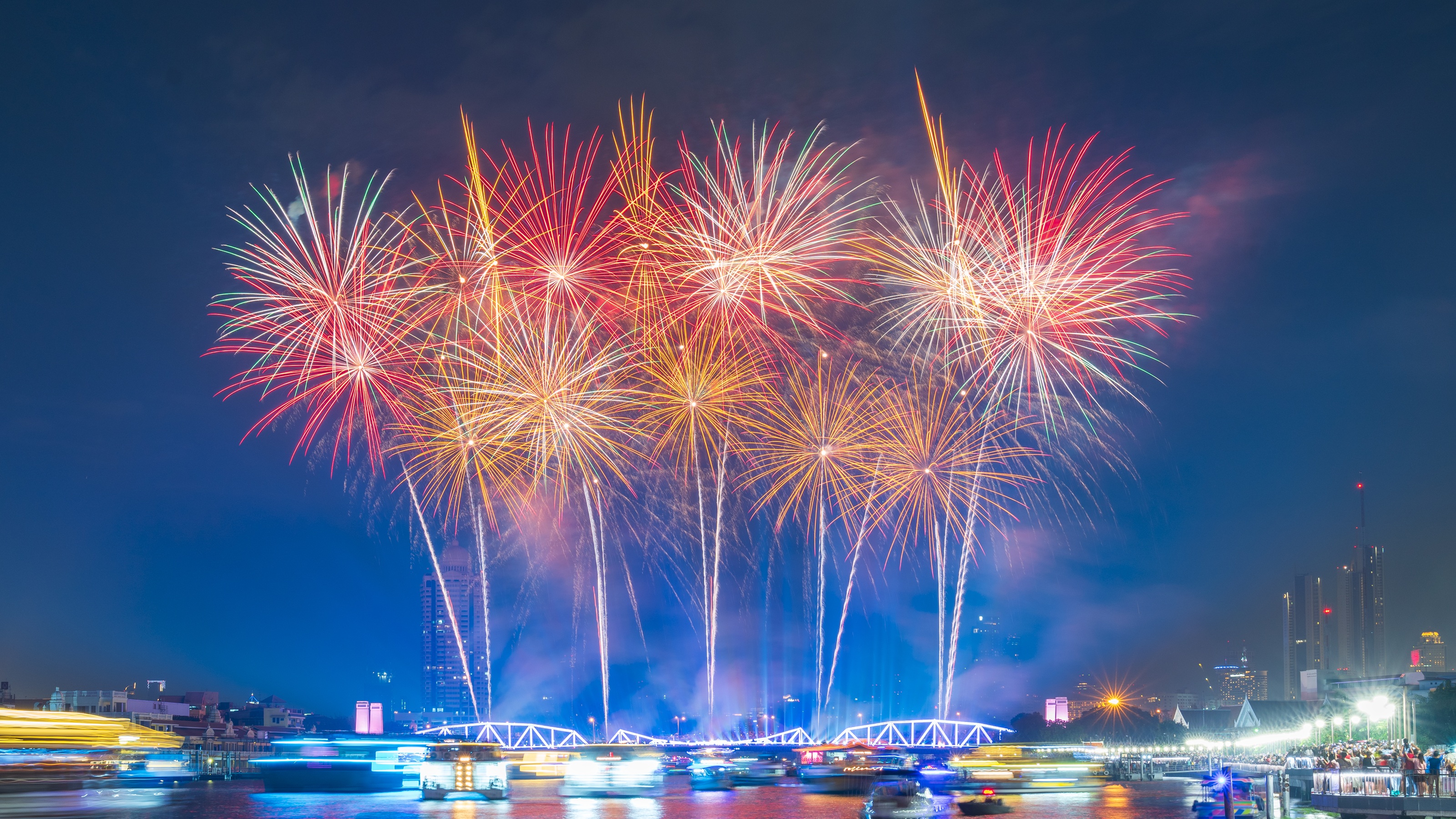 Multiple fireworks exploding over a harbor.
