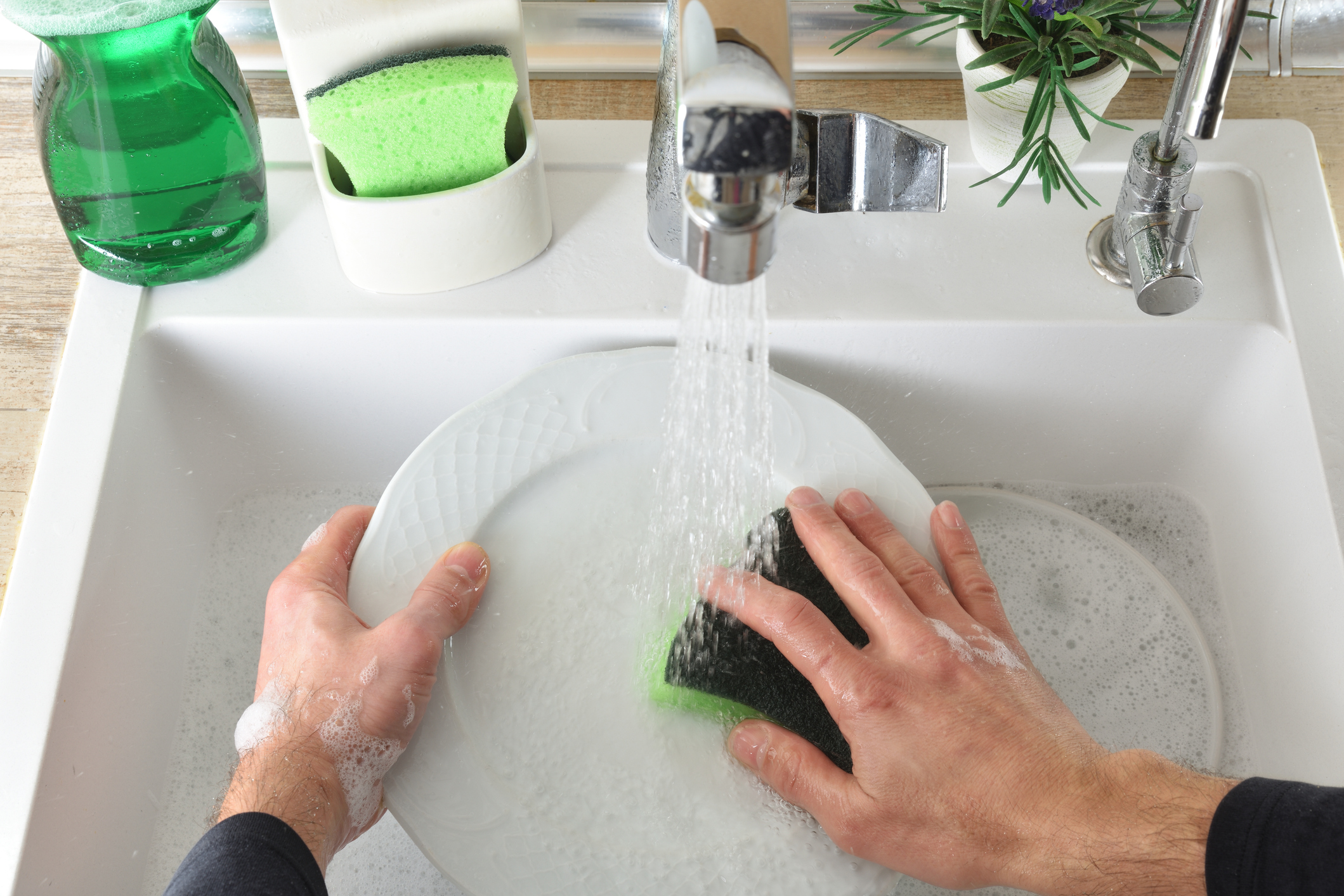 A person handwashing a dish under running water.