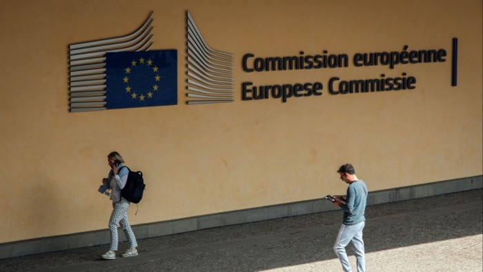 Two people walk past the European Commission building in Brussels, one on the phone and the other looking at a device.