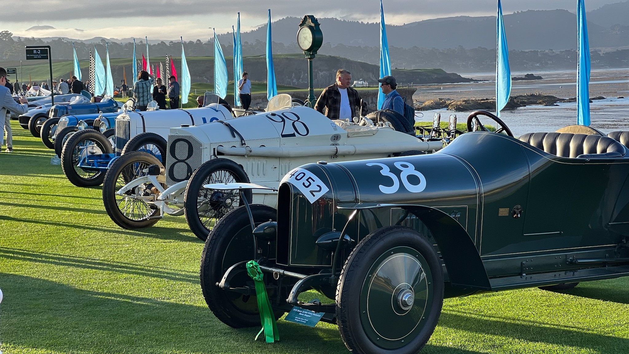 Early 20th century convertible cars with the Califronia coast in the background.