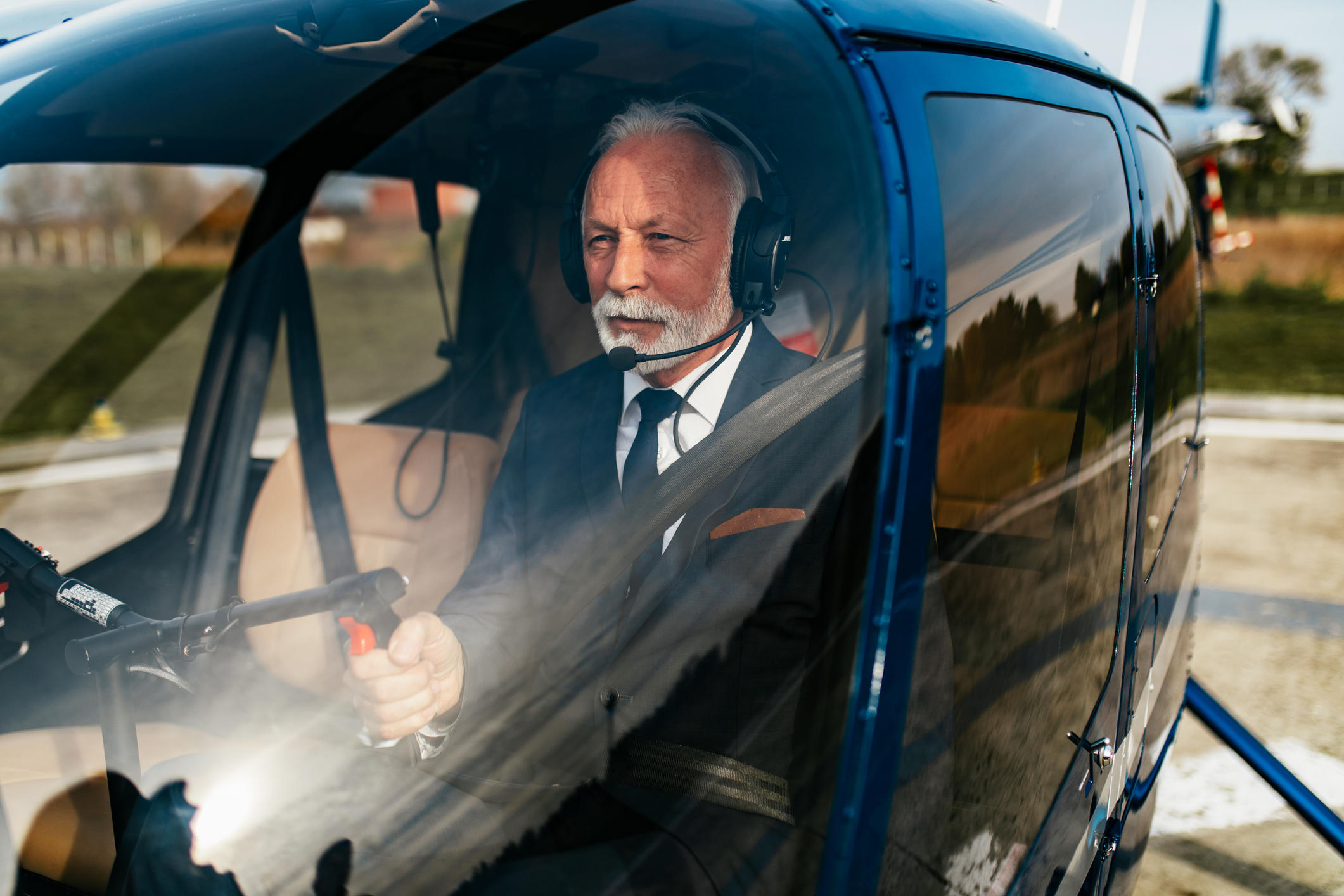 Handsome wealthy senior businessman sitting in his own air transport chopper or helicopter and preparing to fly on business meeting.