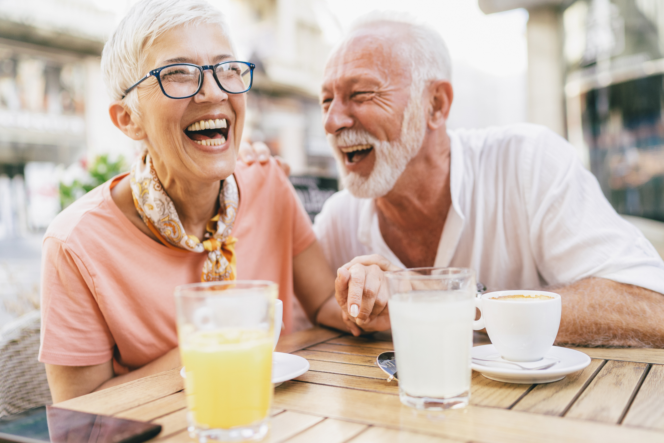 An older couple laughs together, seated at an outdoor table.