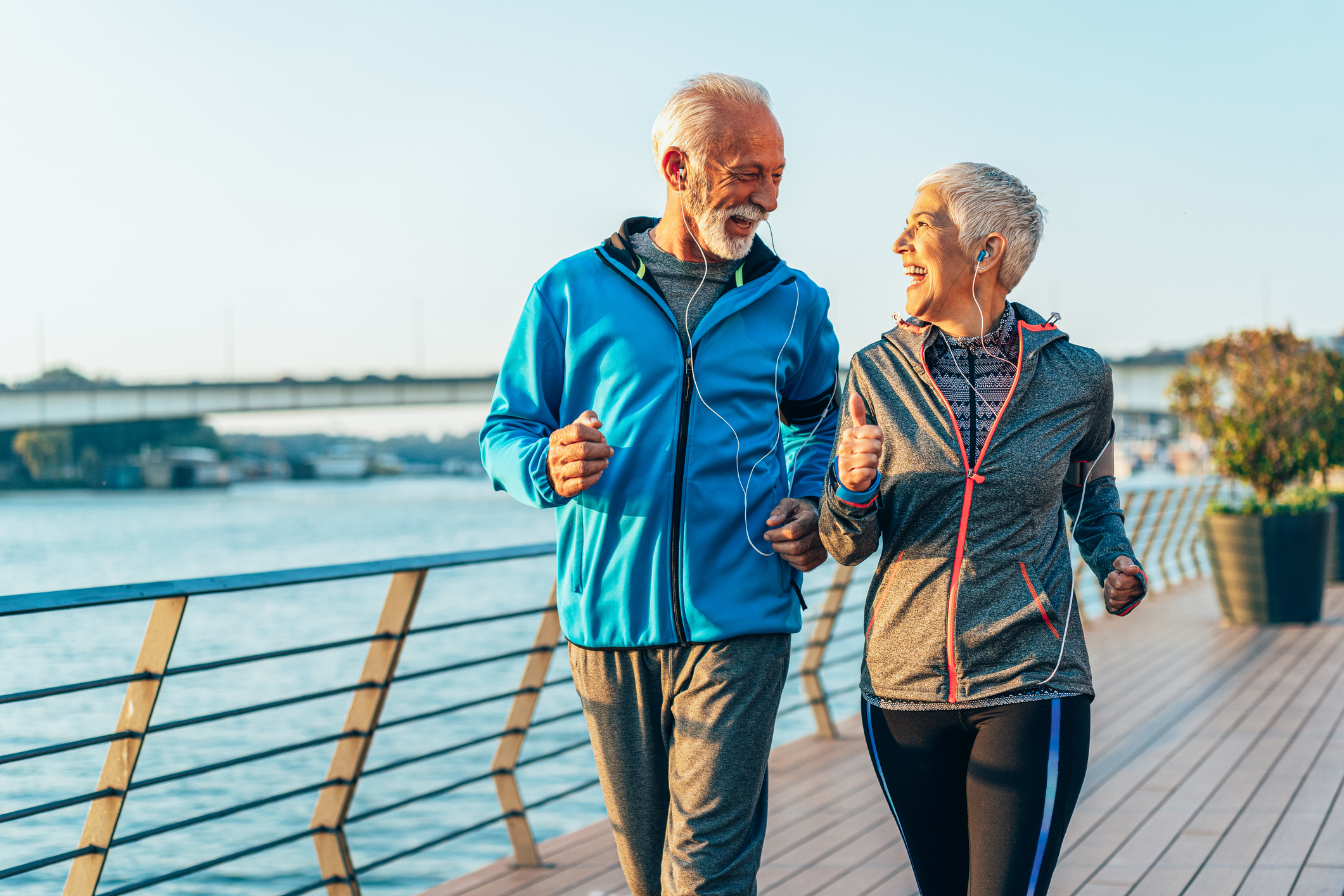 Senior couple in sports clothing and sports technologies jogging together across the bridge.