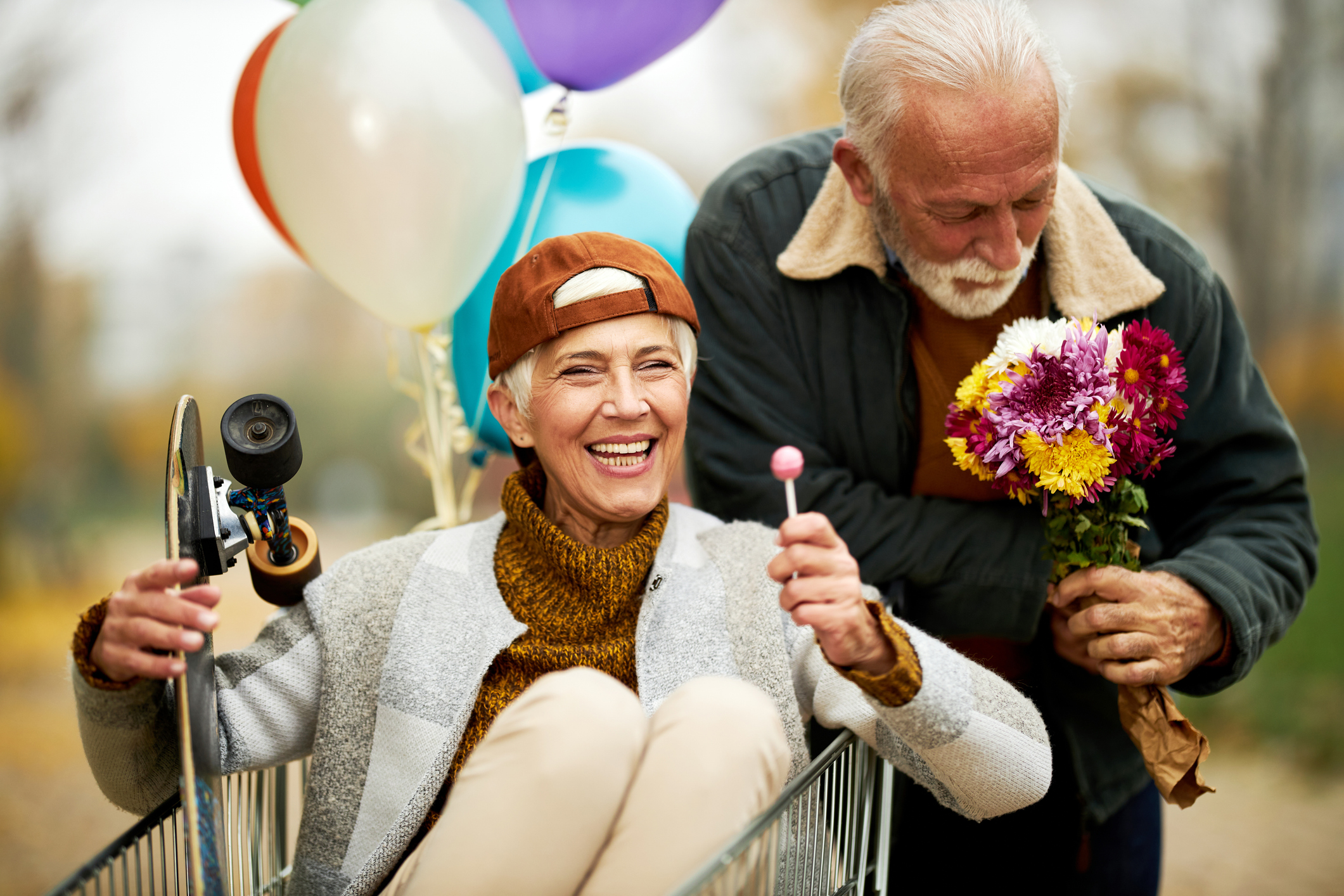 Happy senior woman having fun while being pushed by her husband in shopping cart during autumn day in nature.
