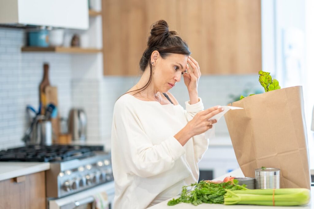 A person in a kitchen looking at a grocery list.