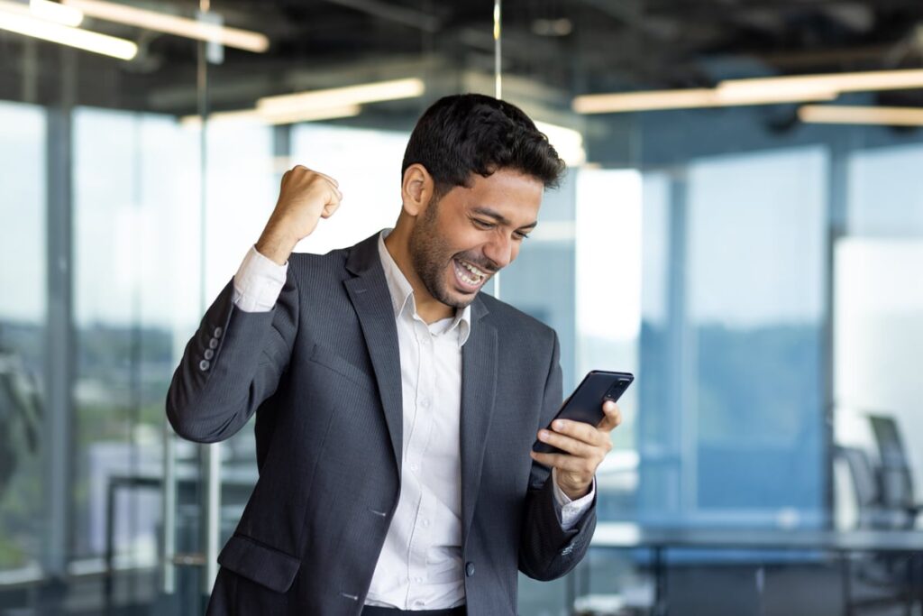 An excited person looking at their smartphone and pumping their fist.