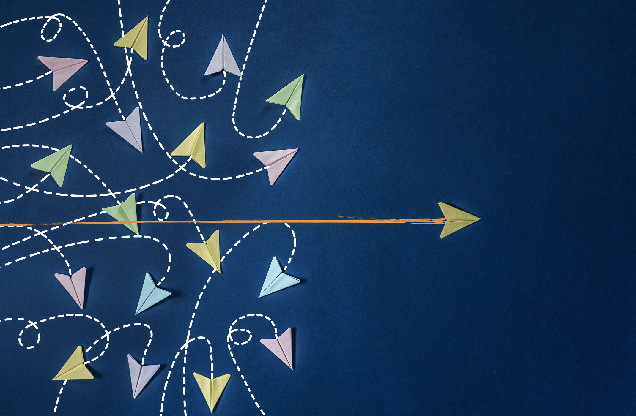 several multi-colored paper airplanes going in all directions with a yellow airplane flying straight out of the chaos