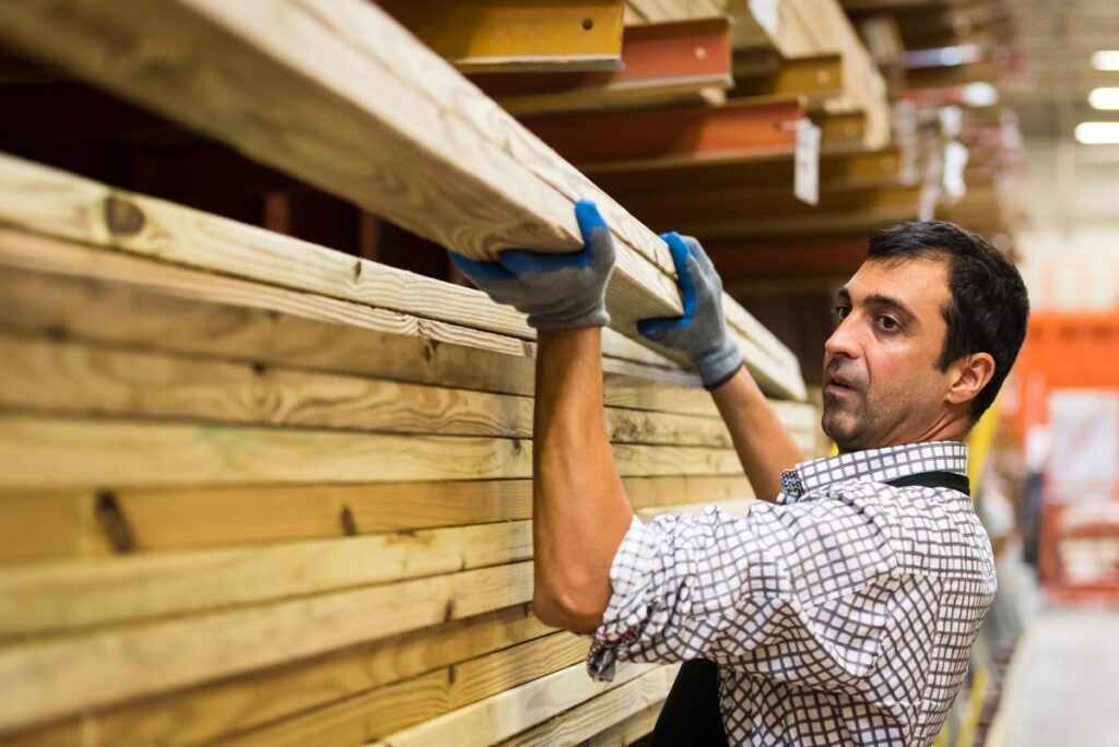 Employee removing two long, unfinished boards from the top of a stack of boards in a home improvement store.
