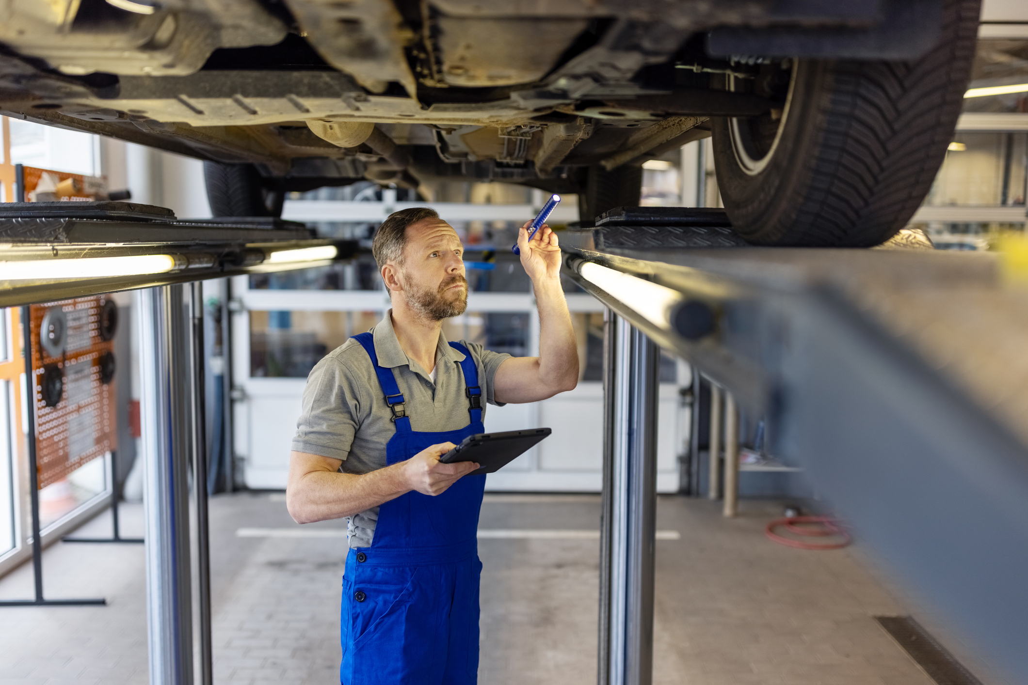 A mechanic inspects the undercarriage of a car at a repair shop.