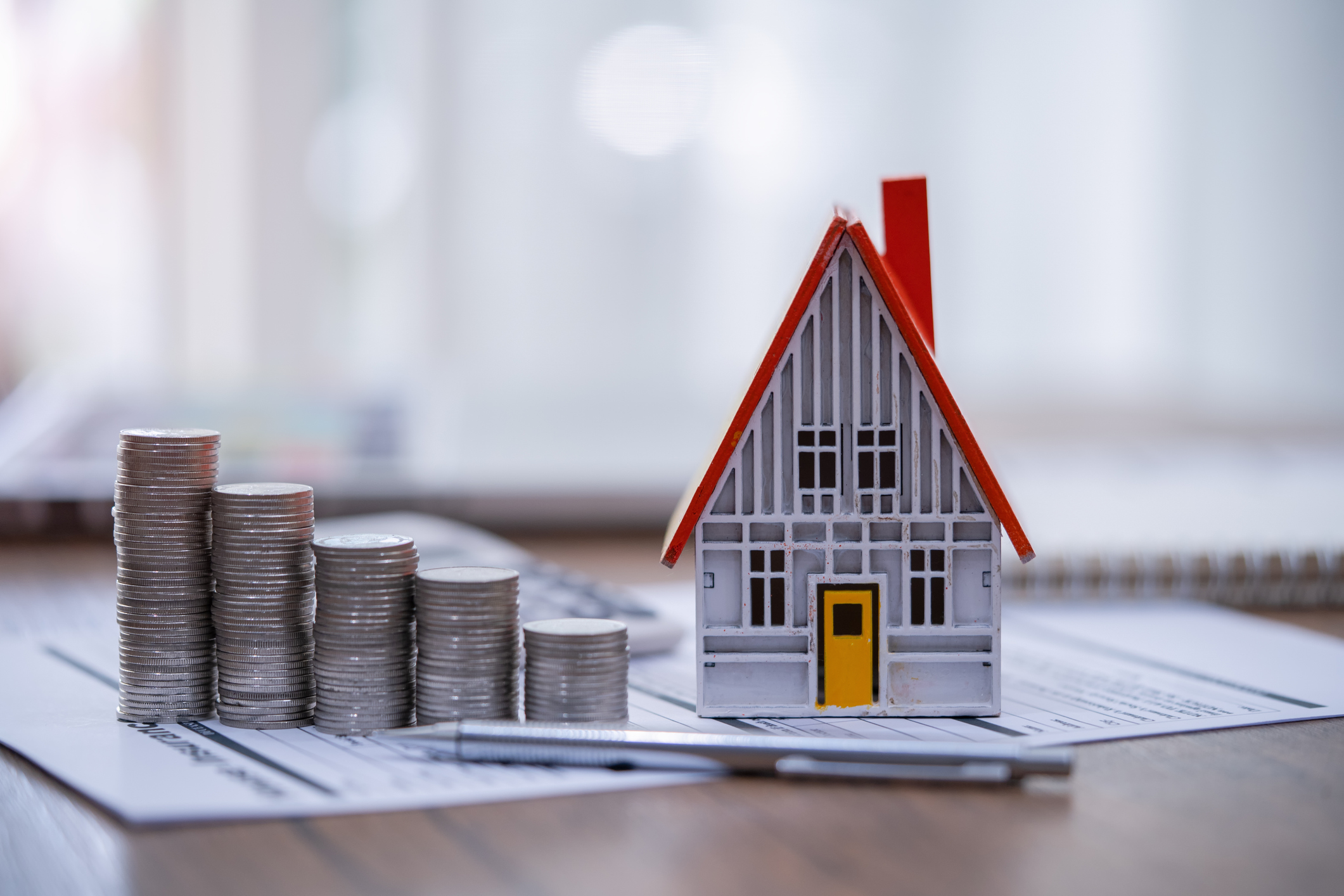 rendering of a mini model house next to stacks of coins on paper