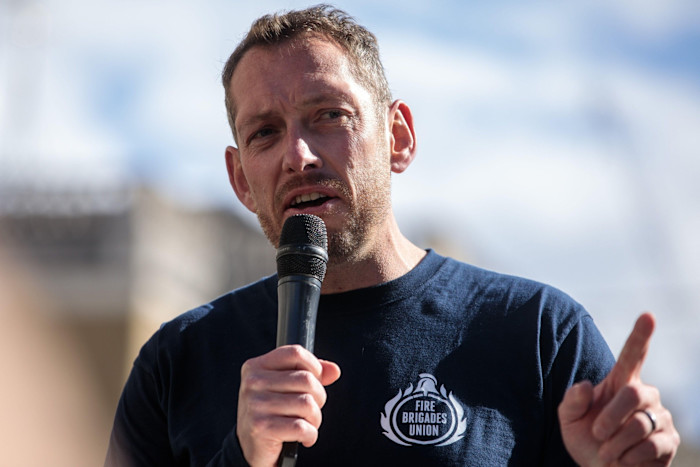 Steve Wright, General Secretary of the Fire Brigades Union, speaks into a microphone and gestures while addressing a crowd