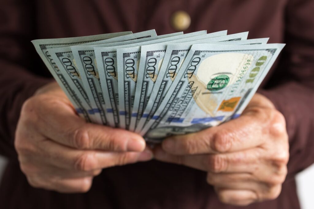 A person fans out ten $100 bills in their hands.