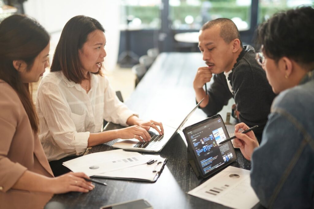 Four people analyzing data on laptops and paper.
