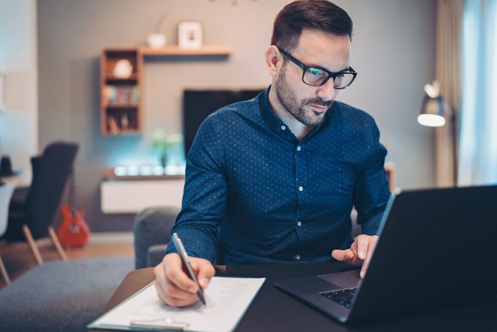 An investor takes notes while studying something on a laptop.