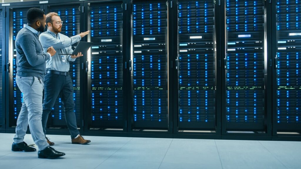 Two people looking at a row of computing servers.