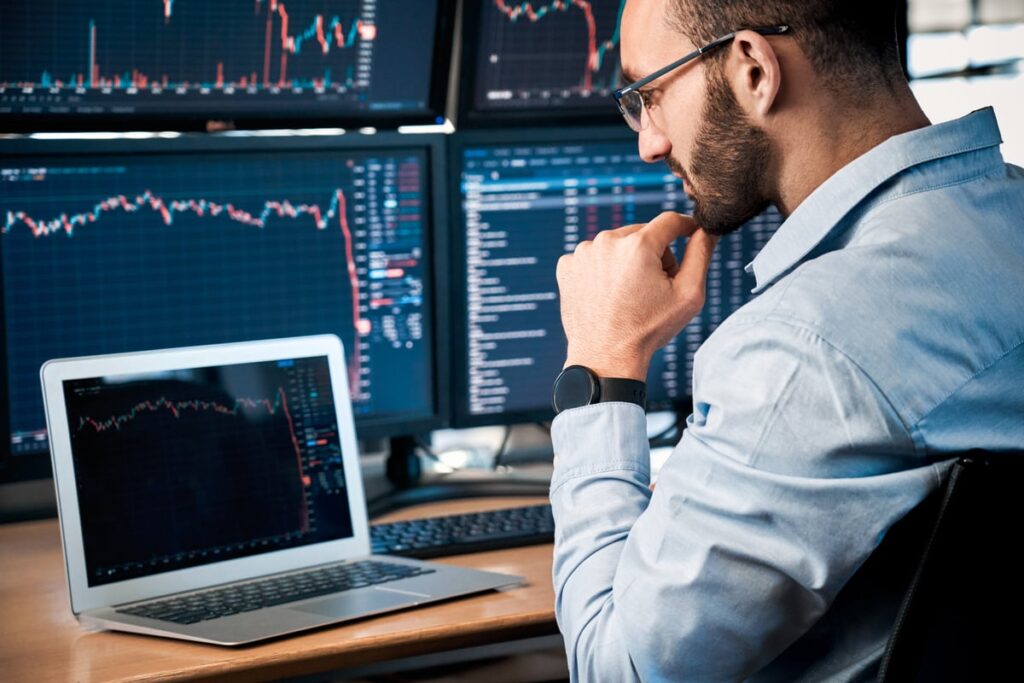 Analyst analyzing stock charts simultaneously on laptop and desktop screens.
