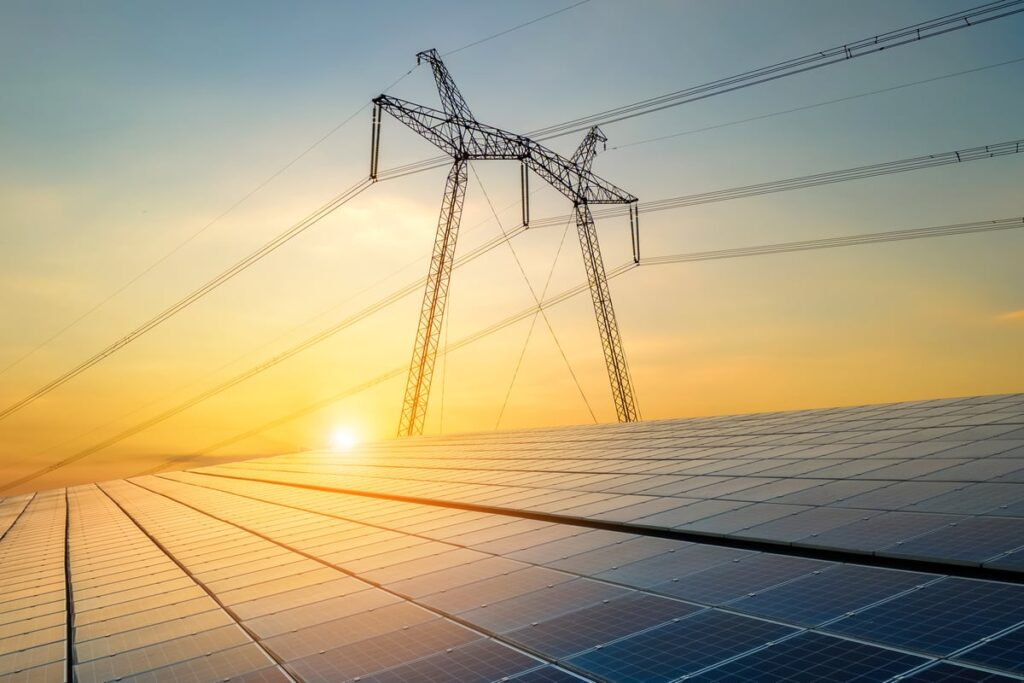 Solar panel with power lines and setting or rising sun in the background.