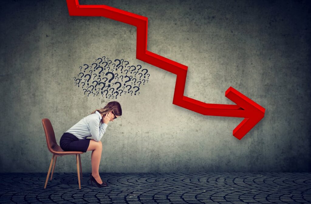 Woman in chair surrounded by question marks under a large red arrow trending down.