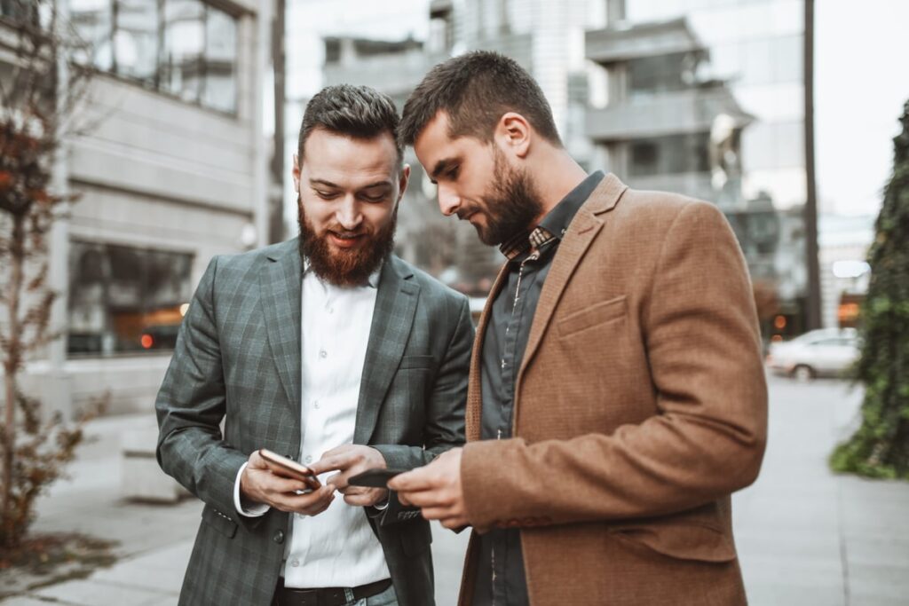 Two investors standing outdoors look at something on a smartphone.