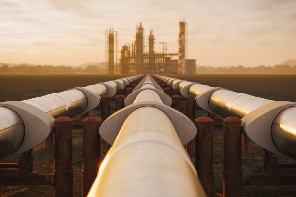 Industrial pipelines stretching across the landscape toward a refinery complex in the distance.