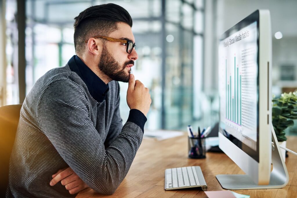 An investor sits at a desk while considering a bar chart displayed on a computer.