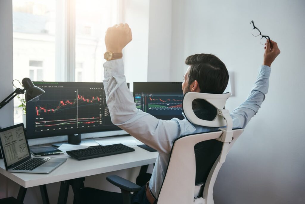 Happy investor looking at stock charts on a computer screen.