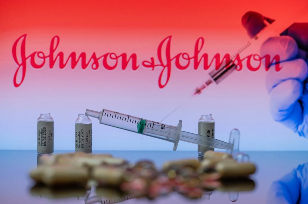 A hand with a syringe with Johnson & Johnson's logo in the background.