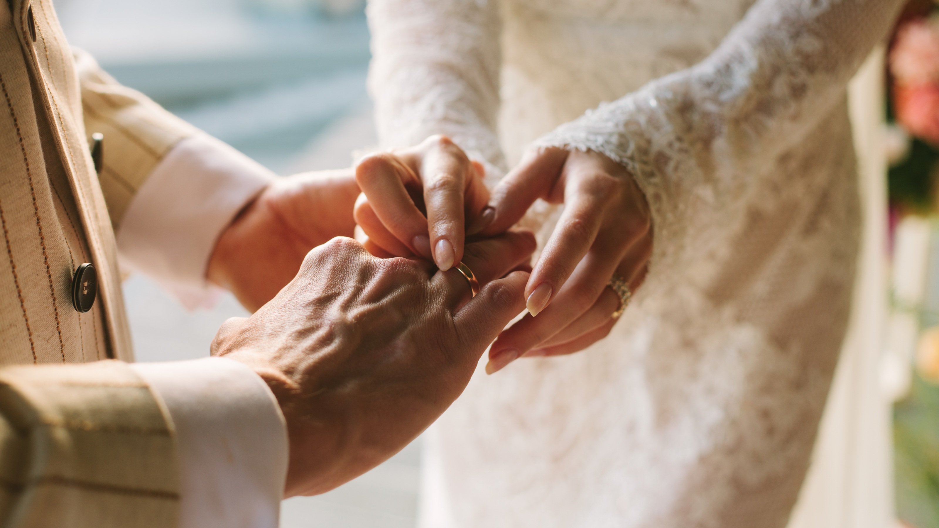 A bride slides a wedding ring onto her groom's hand.