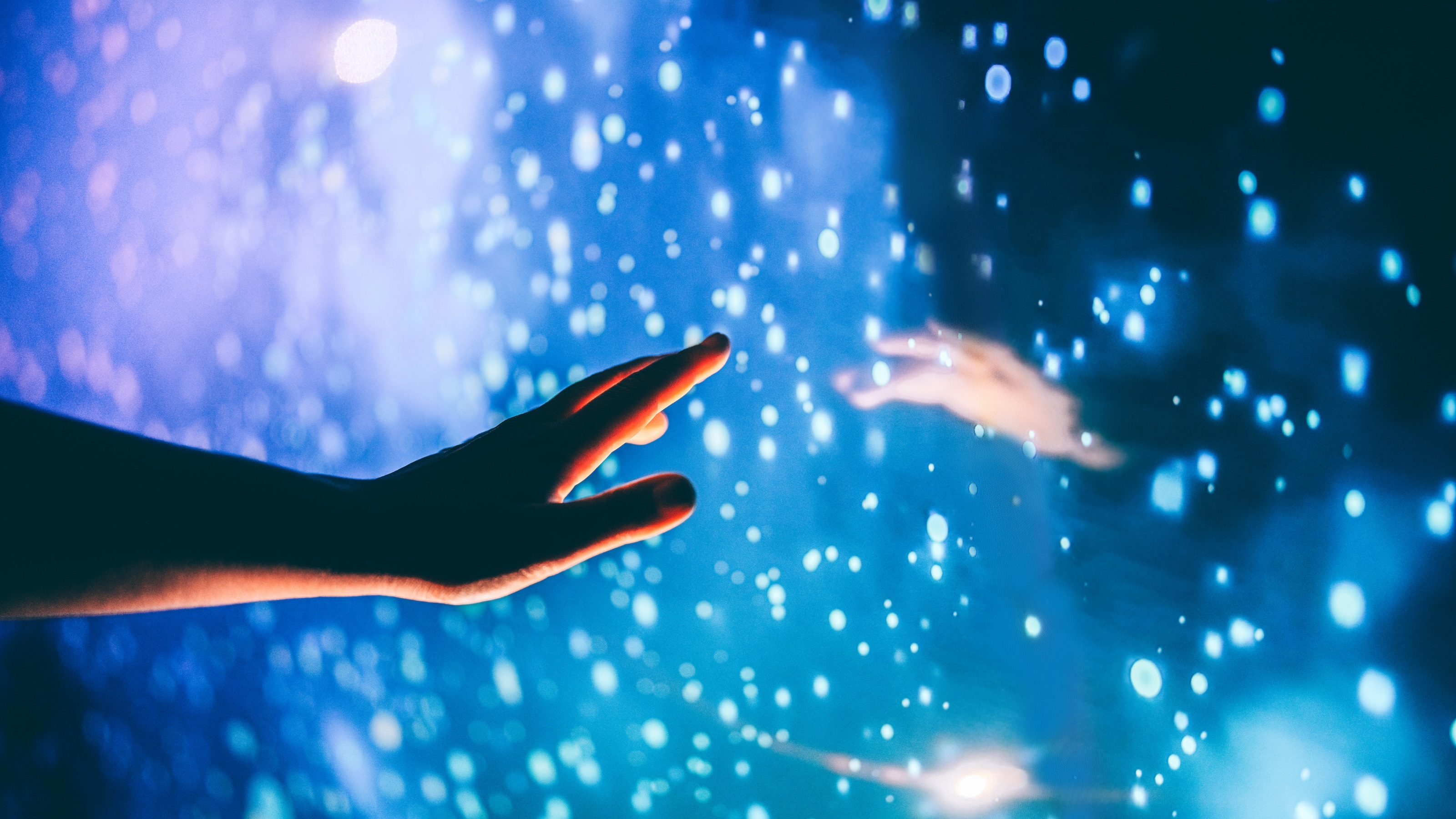 A hand reaches toward a hand on the other side of a starry-looking landscape.